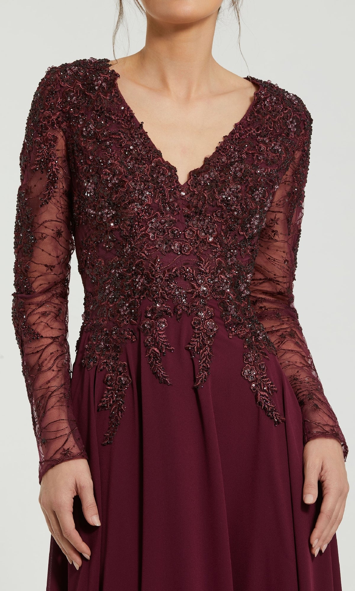 A woman wears the Mac Duggal 20388 long sleeve special occasion dress in burgundy, featuring intricate bead and lace detailing on the bodice and sleeves.